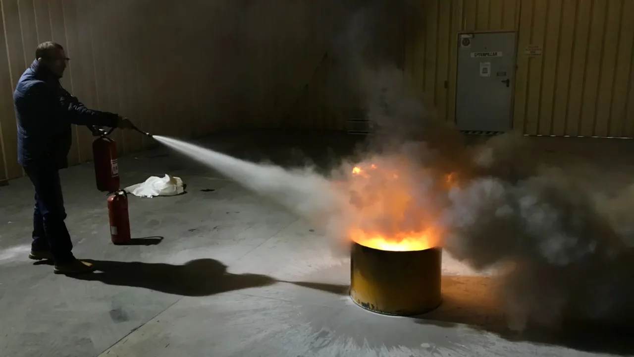 Fire extinguisher training. A man using a fire extinguisher in a dark room.